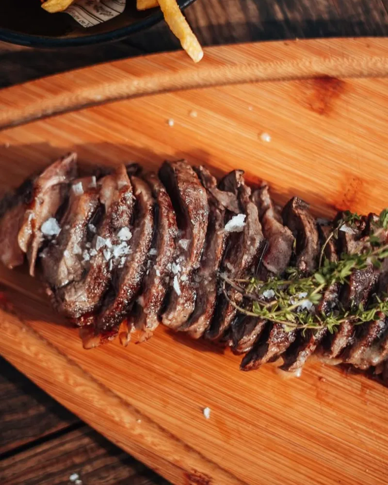 Carne a la brasa cortada sobre tabla de madera, con tomillo