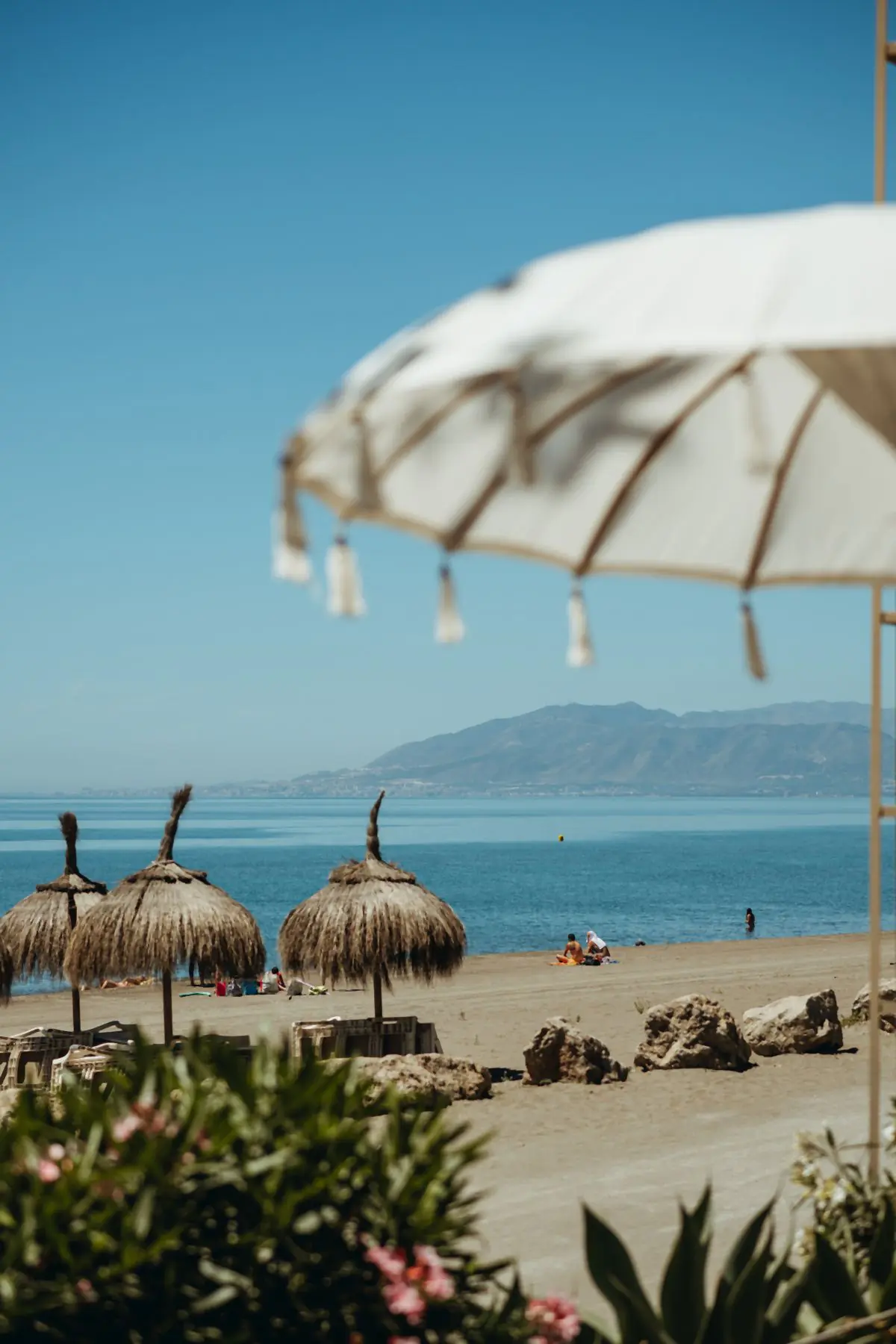 La playa con las sombrillas de paja y la costa al fondo
